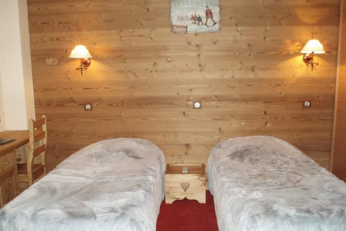 A room with two beds, wooden walls, and two wall-mounted lamps.