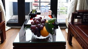 Ein Zimmer mit einem Glastisch, der eine Obstschale, eine Wasserflasche und eine Packung Taschentücher beherbergt. Im Hintergrund ist eine Tür mit Blick auf Gebäude zu sehen.
