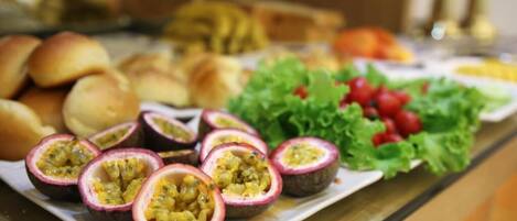 Un bufé con diversas opciones de comida, incluyendo panecillos, fruta de la pasión y una ensalada de lechuga y tomates.