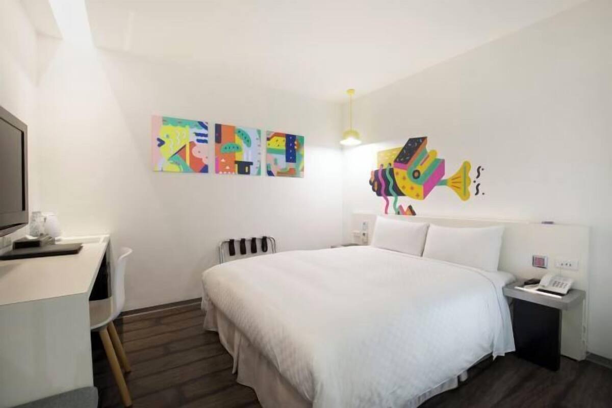 Habitació d'hotel amb un llit, escriptori, cadira, radiador i decoració mural.