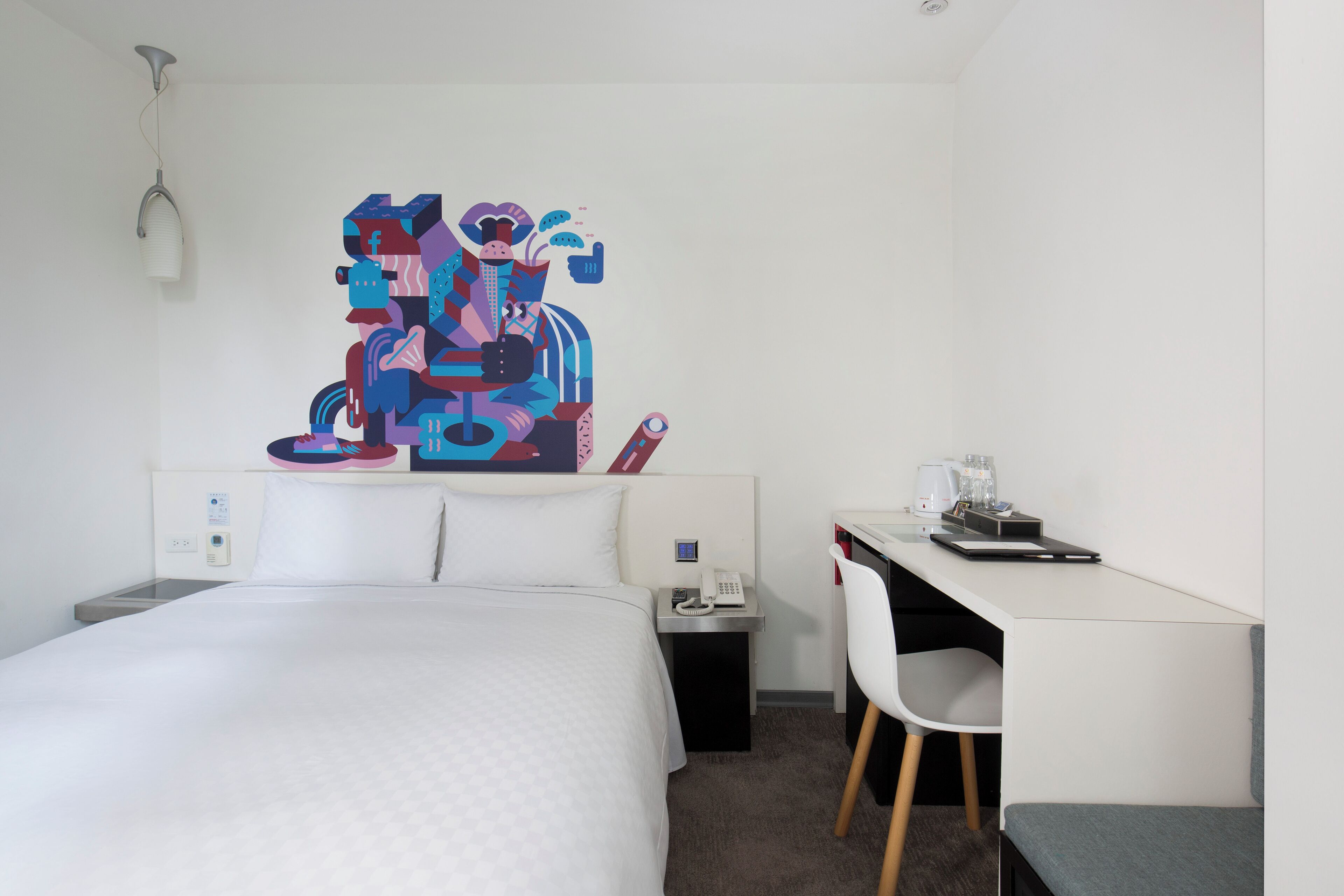 Habitación de hotel con cama, escritorio, silla, mesita de noche y una obra de arte colgada en la pared.