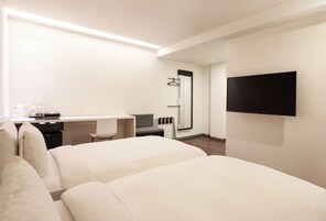 Hotelkamer met twee bedden, een bureau met stoel, een aan de muur bevestigde televisie en een douche.
