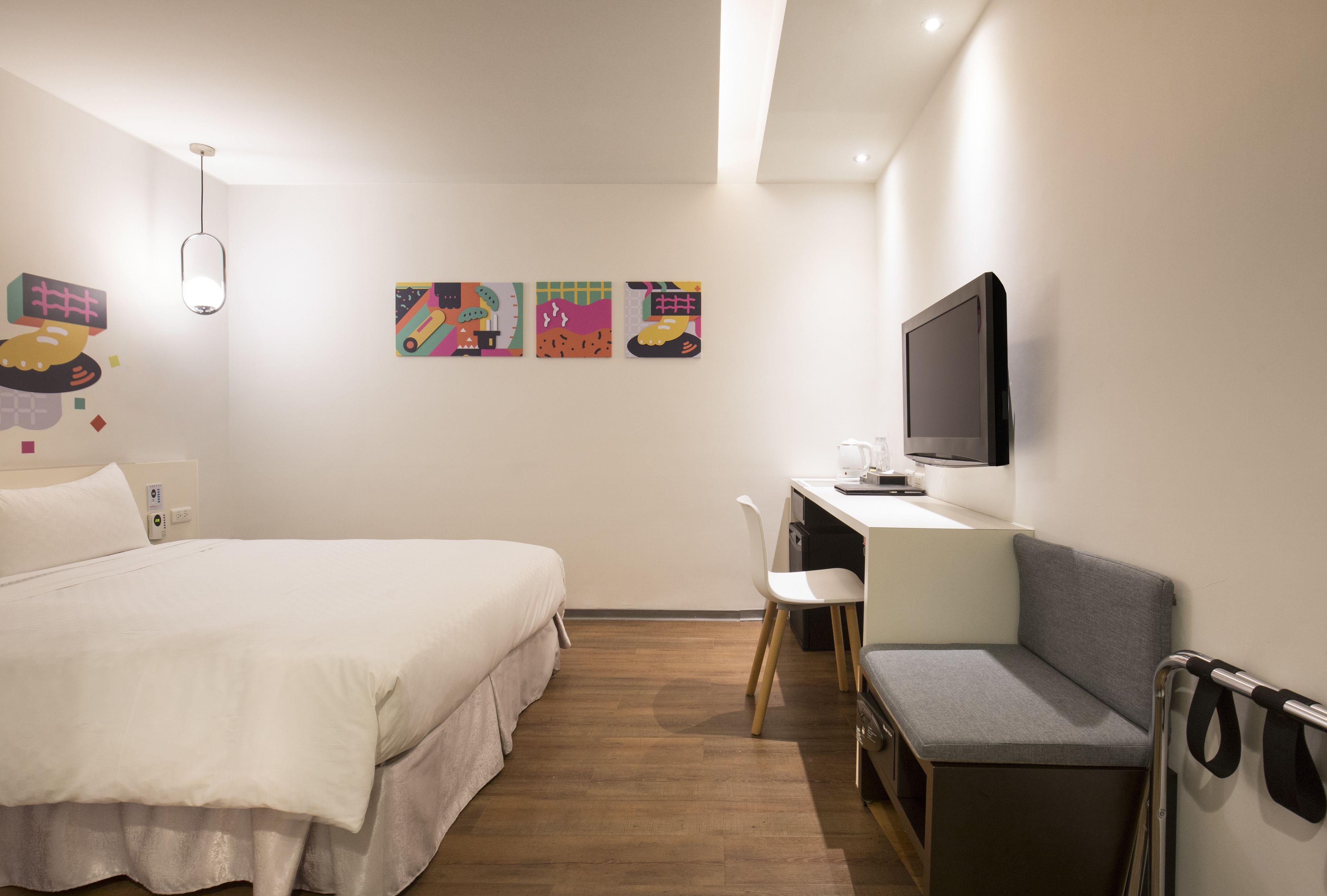 Una habitación de hotel con una cama, un escritorio, una silla, un televisor y decoración en la pared.