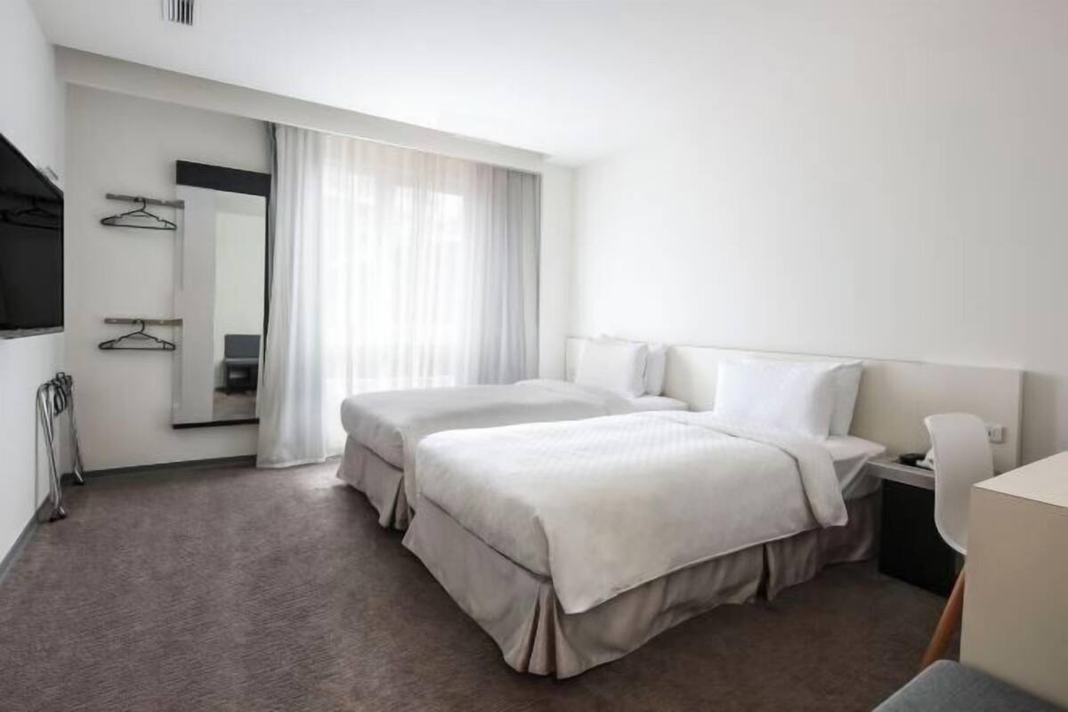 Habitació d'hotel amb dos llits, un escriptori, una cadira, un televisor i un mirall.