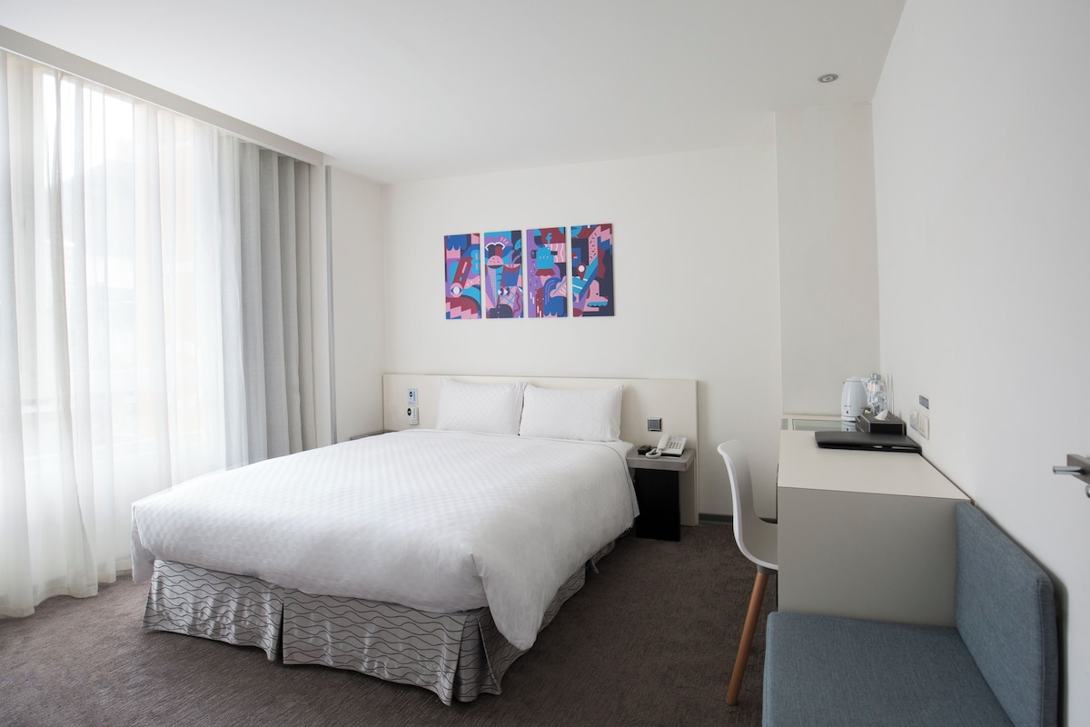 Une chambre d’hôtel avec un grand lit, un bureau avec une chaise, un téléphone et une machine à café.