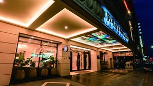 A hotel entrance with a modern design, featuring a glass facade, a digital signboard, and a well-lit entrance area.