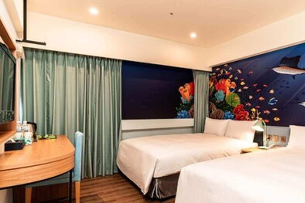 Una camera d'albergo con due letti, una scrivania e un murale raffigurante una scena subacquea.