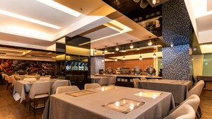 A restaurant with multiple tables and chairs, a kitchen area, and a decorative wall.