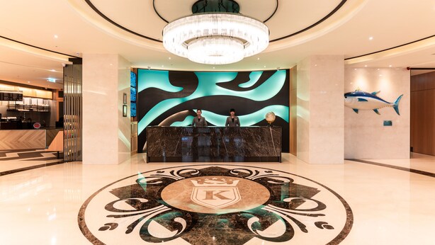 A hotel lobby with a large chandelier, a reception desk, and a decorative floor design.