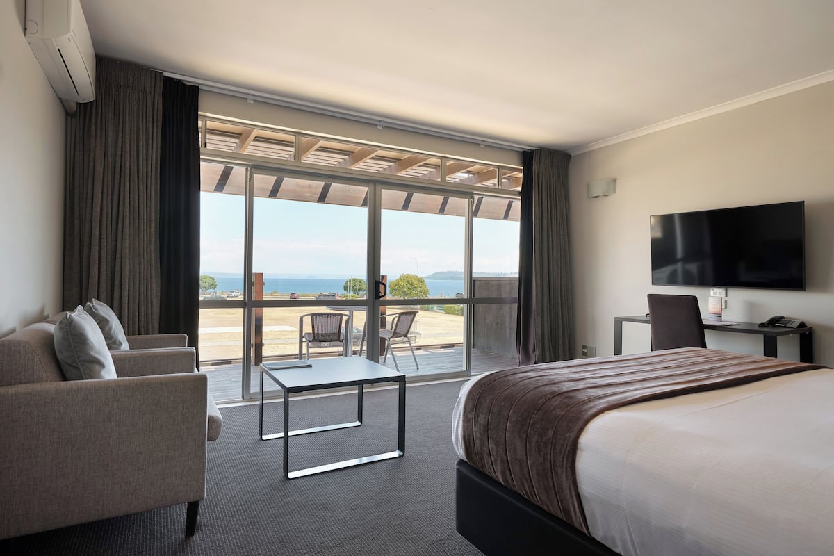 Een hotelkamer met een bed, een bureau, een stoel, een bank en een groot raam met uitzicht op zee.