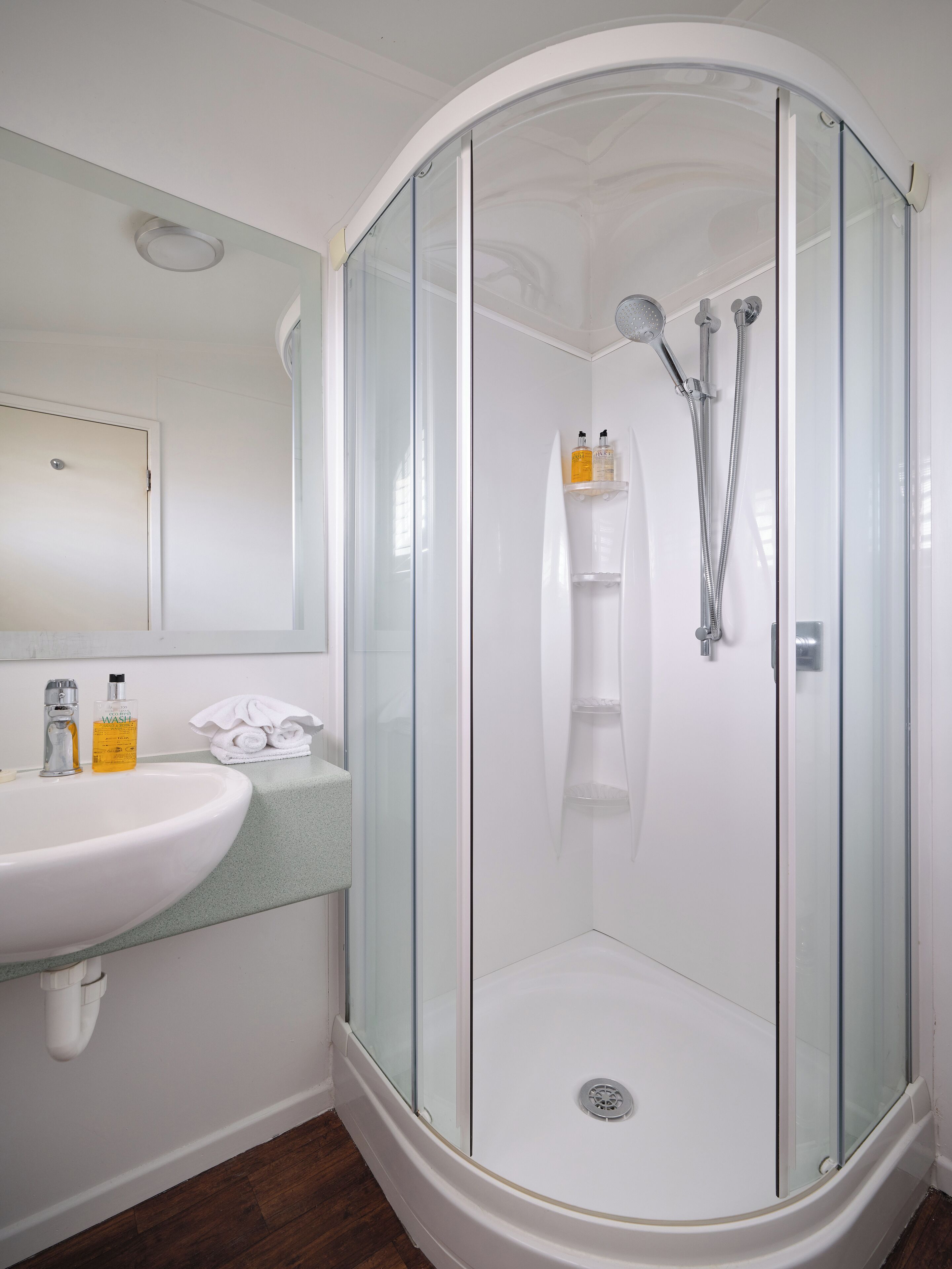 A modern bathroom with a glass-enclosed shower, a white sink, and a mirror above the sink.
