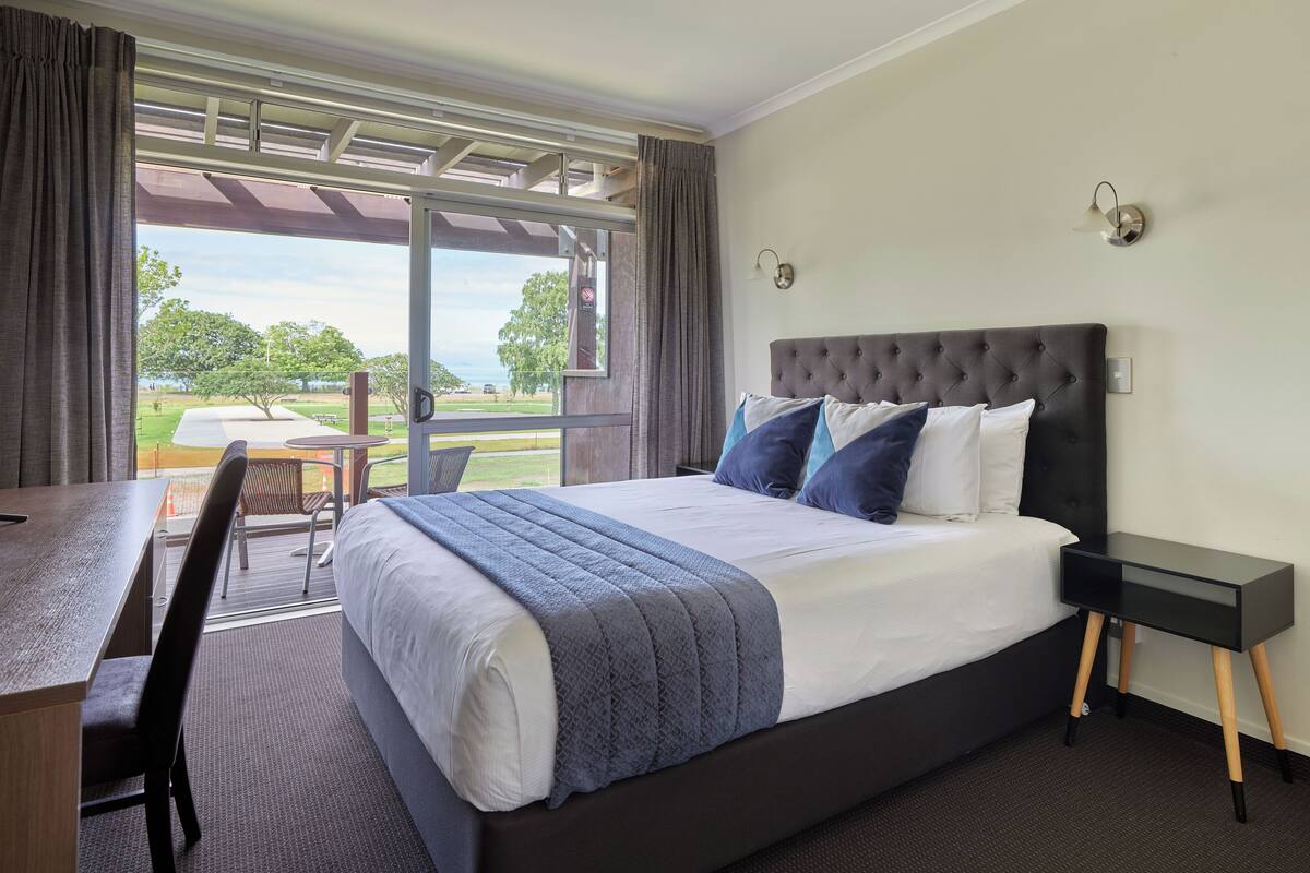 Een hotelkamer met een groot bed, een bureau en uitzicht op een park en een wateroppervlak.