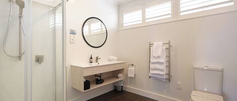 A modern bathroom with a glass shower enclosure, a white sink with a mirror, a toilet, and a towel rack.