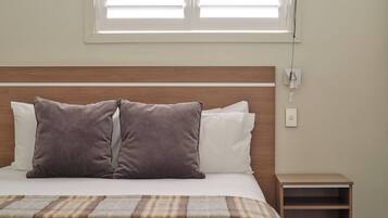 Una cama bien hecha con dos almohadas, una mesita de noche y una ventana con persianas.