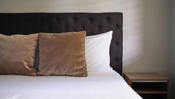 Un letto ben rifatto con testiera imbottita, due cuscini e un comodino in legno accanto.