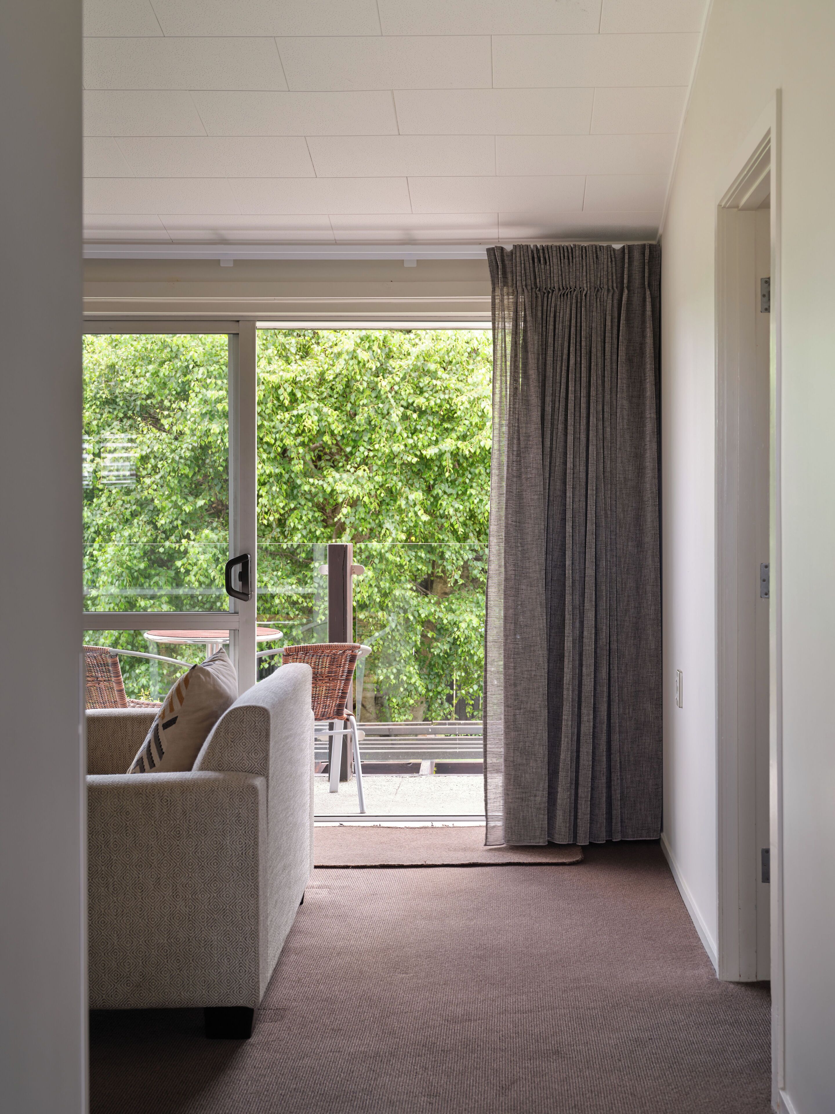 A room with a large sliding glass door leading to a balcony with wicker furniture and a view of greenery.