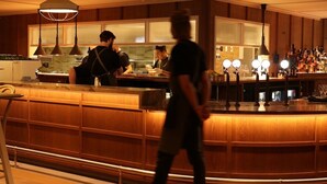 Zona de bar con mostrador de madera, iluminación colgante y estanterías llenas de botellas.