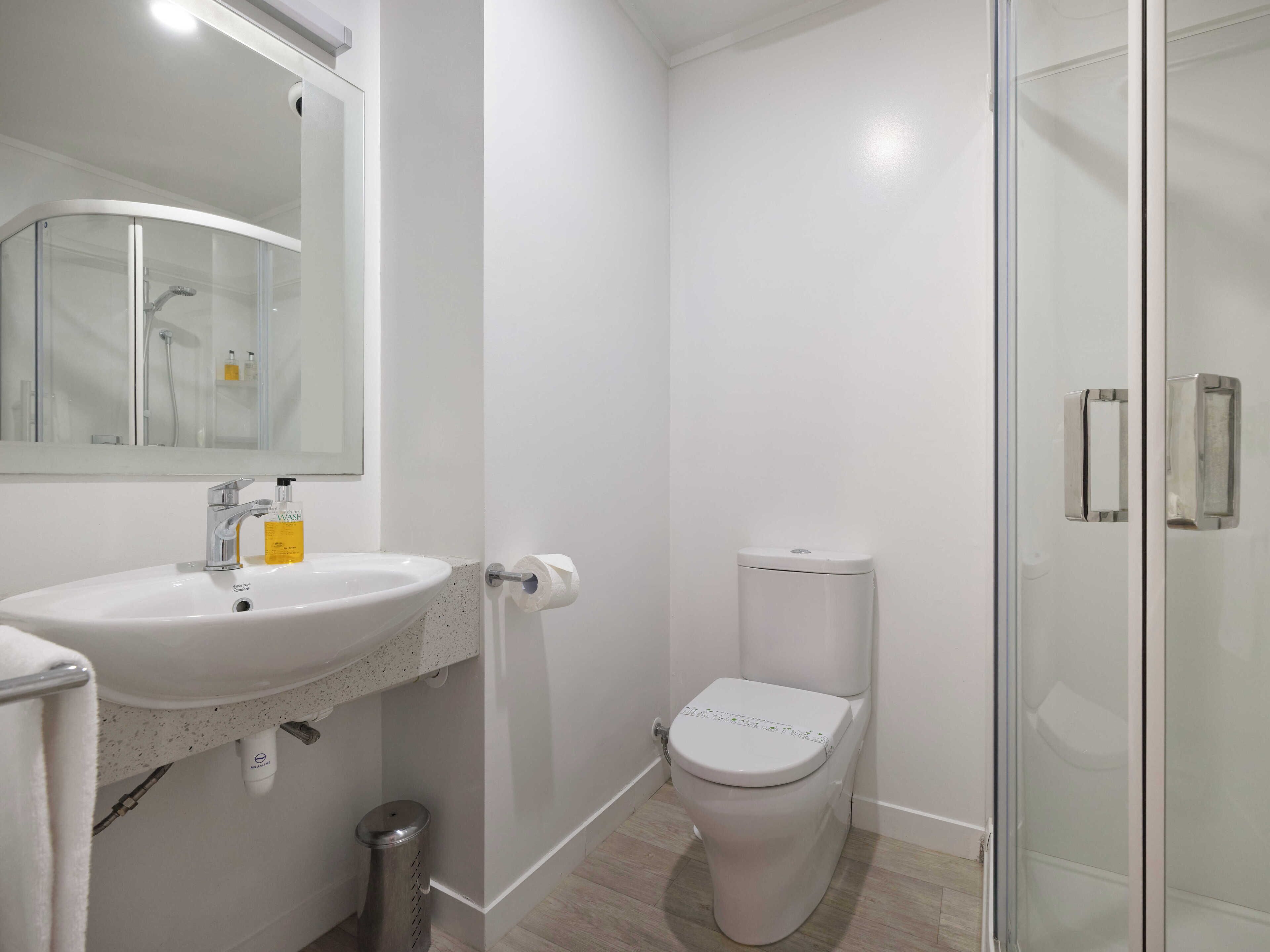 A modern bathroom with a white sink, toilet, and glass shower enclosure.