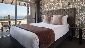 Habitación de hotel con una cama grande, vistas a la playa y un papel tapiz tropical.
