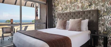 A hotel room with a large bed, a view of the beach, and a tropical wallpaper.