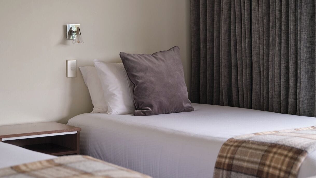 A hotel room with a bed, a nightstand, a lamp, and a window with curtains.