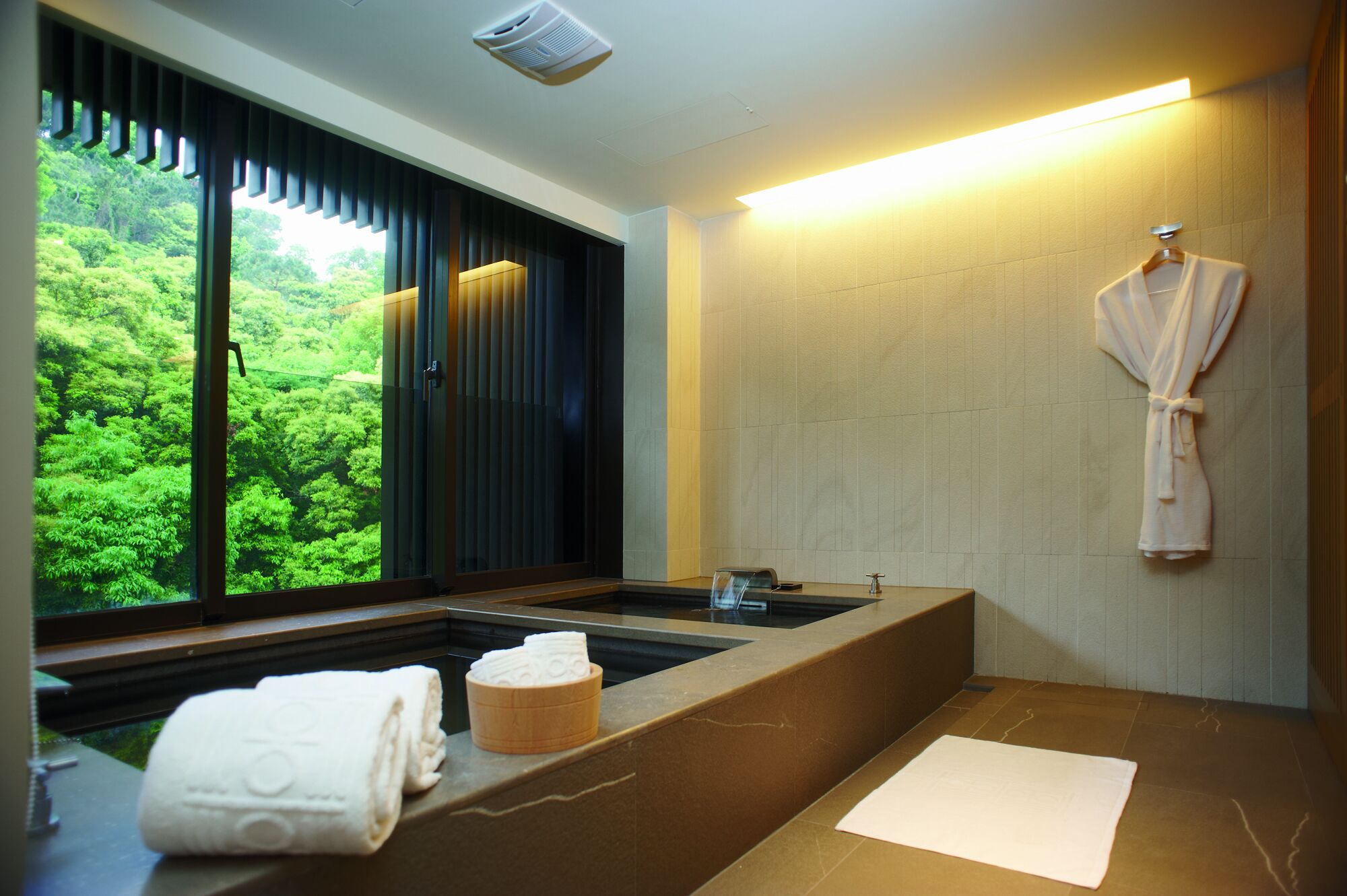 A modern bathroom with a large window, a bathtub, a towel rack, and a robe hanging on the wall.