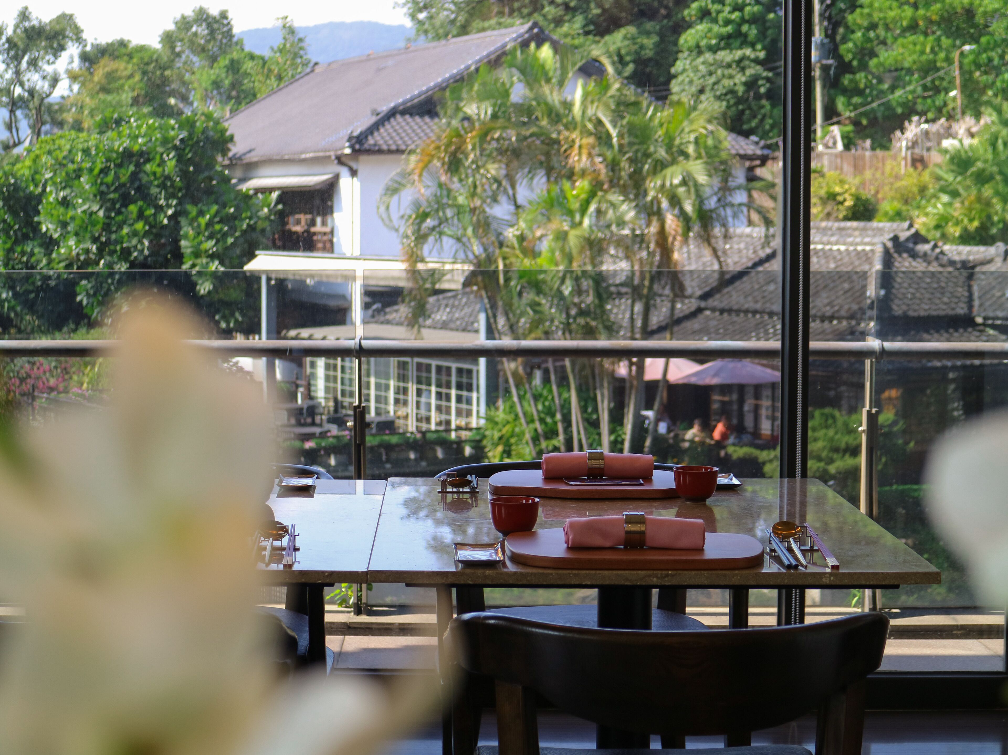 A dining table with a view of a traditional house and lush greenery.
