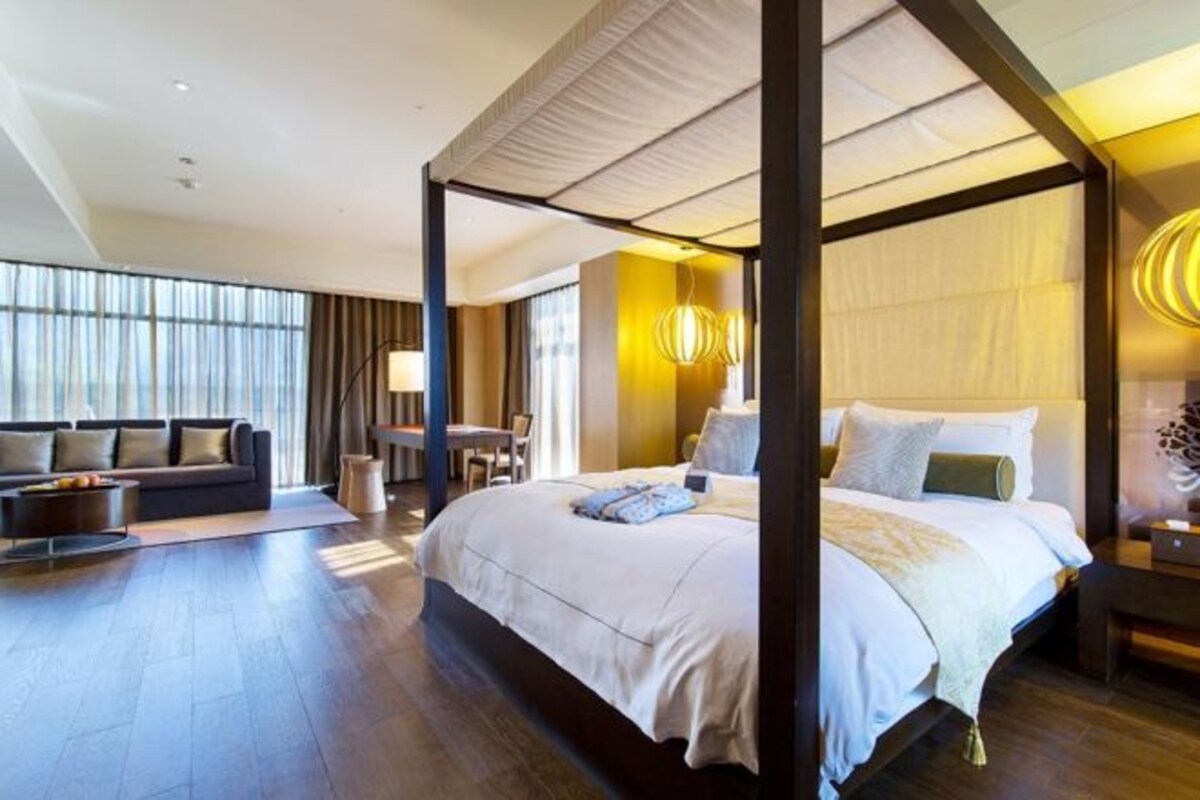 A spacious bedroom with a four-poster bed, a sitting area with a sofa, and a dining table.
