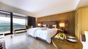 A hotel room with a large bed, a dining table with fruits, and a view of the outdoors.