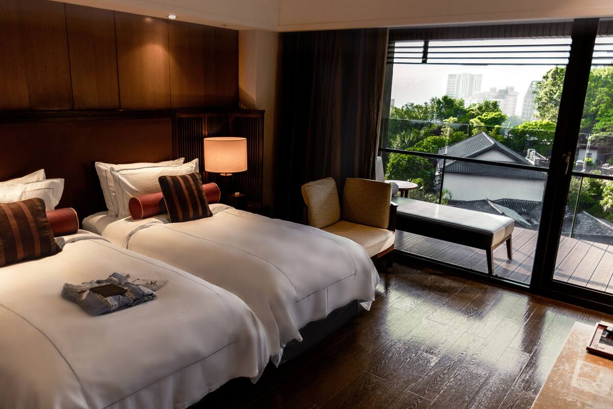 Quarto de hotel com duas camas, um sofá, uma mesa e vista para um edifício tradicional e paisagem urbana.