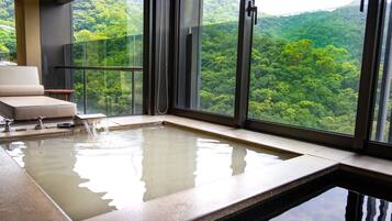 A modern spa area with a hot tub, a cushioned seating area, and a glass railing overlooking a forested landscape.