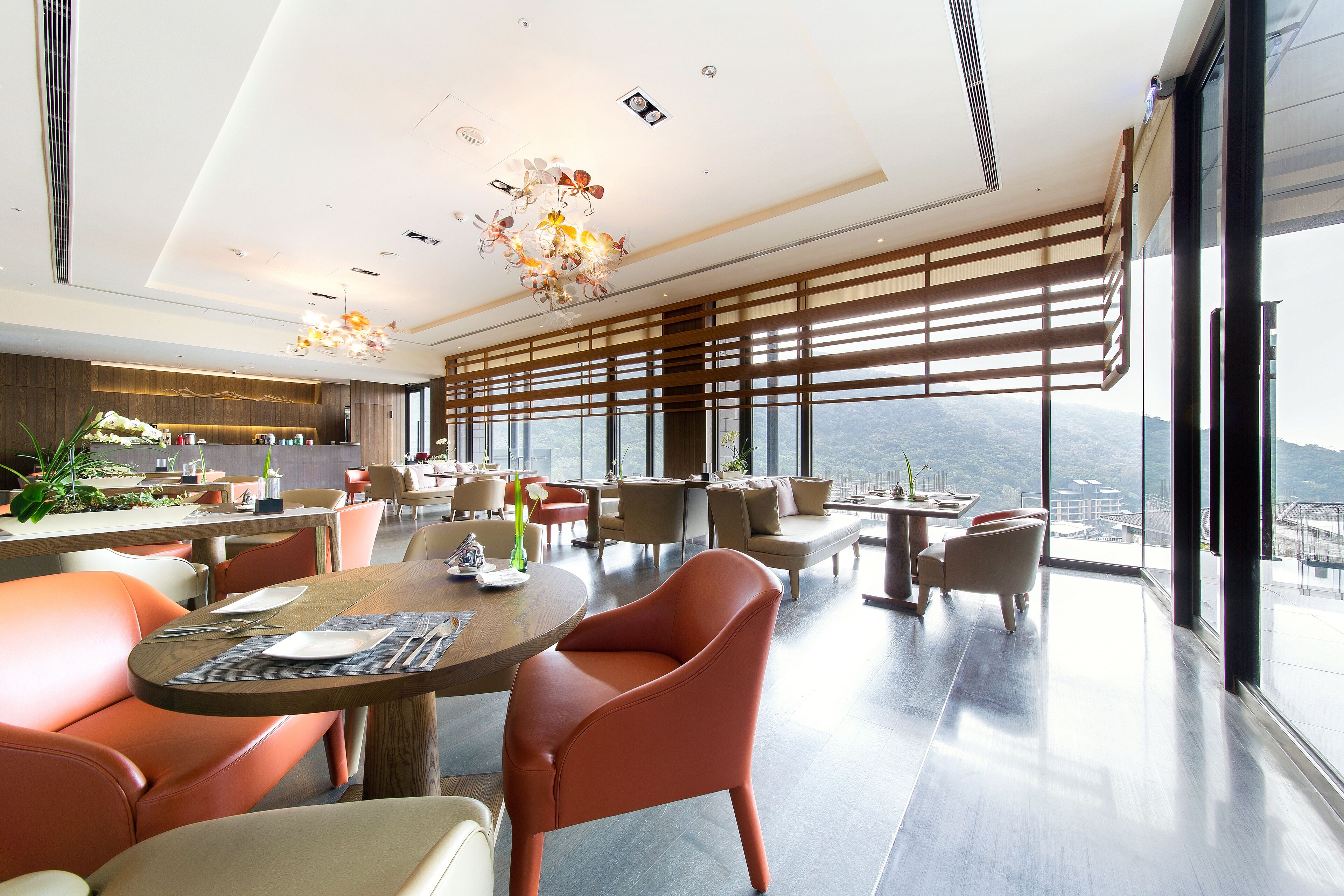 A modern dining area with a high ceiling, large windows, and a view of the cityscape.