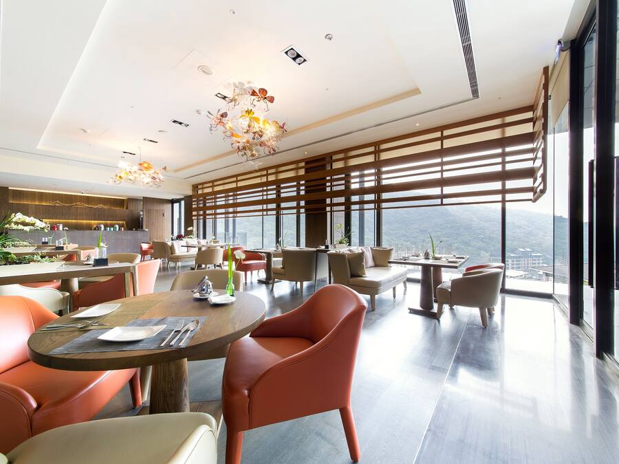A modern dining area with a high ceiling, large windows, and a view of the cityscape.