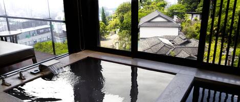 A modern bathroom with a large window, a bathtub, and a view of traditional buildings and greenery.