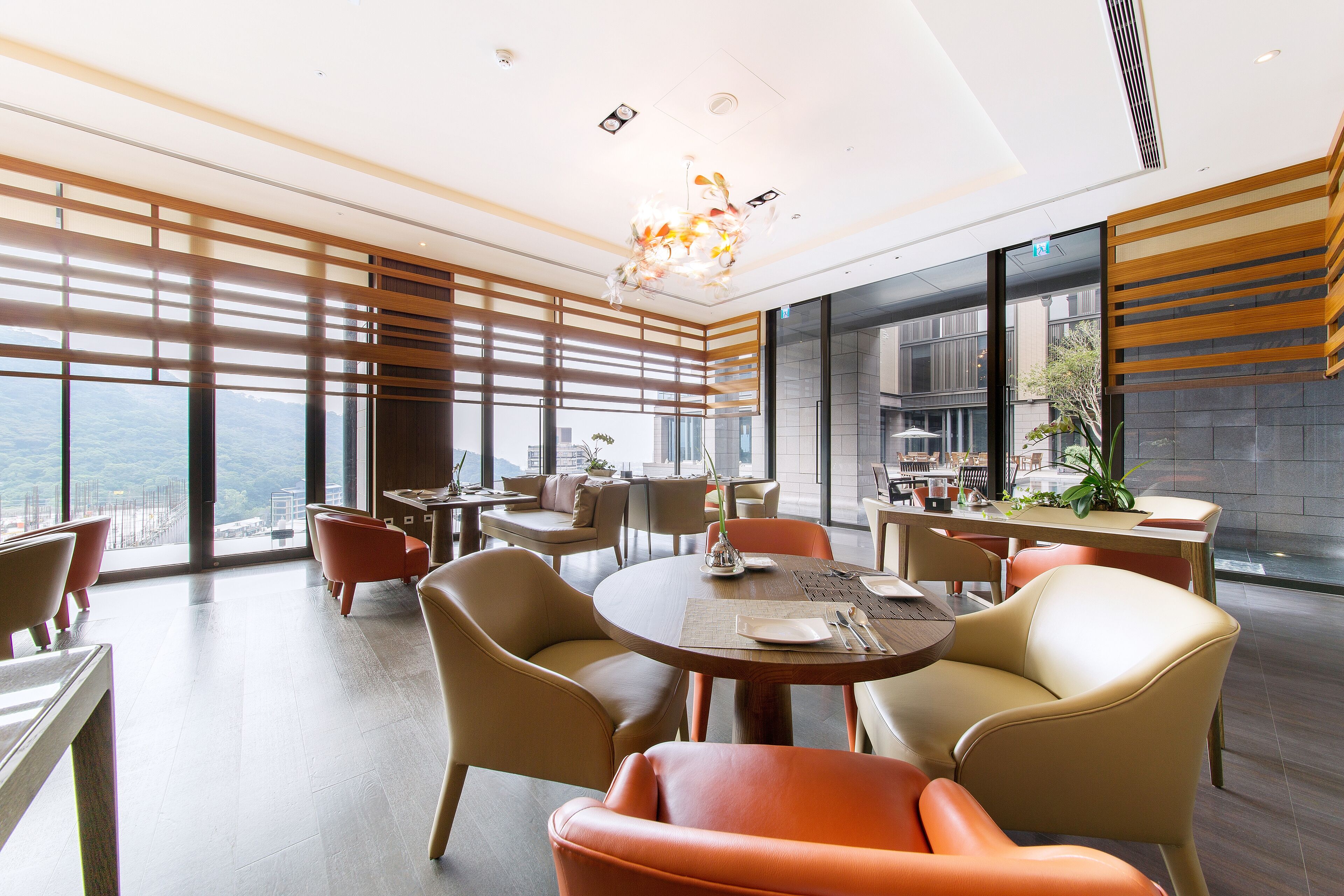A modern dining area with round tables and leather chairs, large windows with a view, and a contemporary chandelier.
