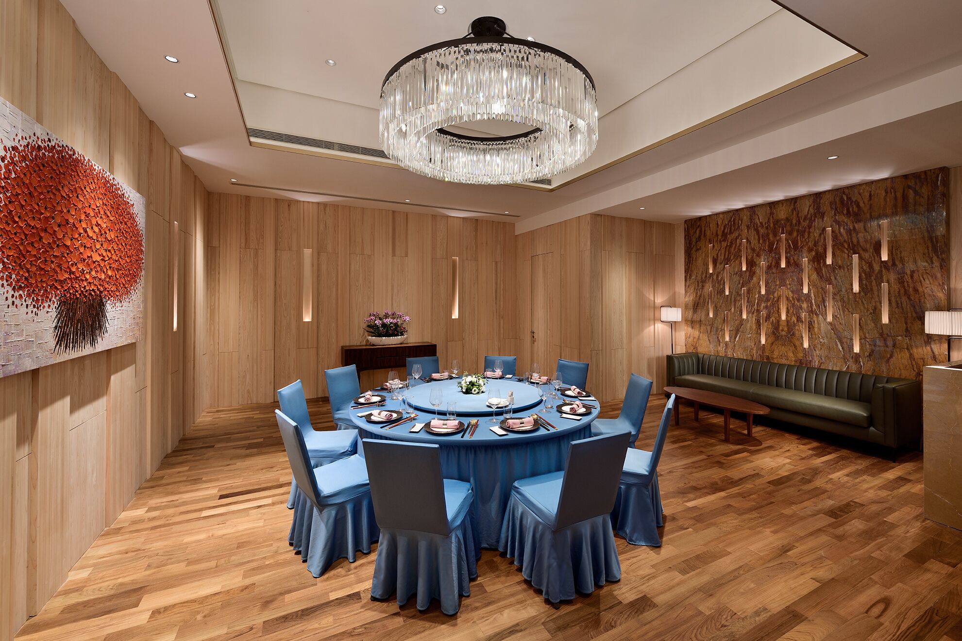 A modern dining room with a round table, blue chairs, and a chandelier.