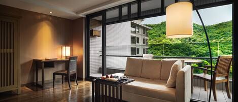 A modern living room with a sofa, a table, and a chair. There is a large window with a view of a building and greenery.