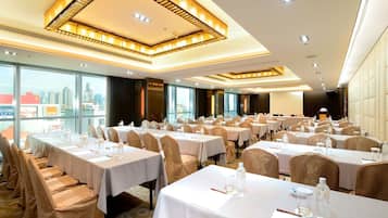 A conference room with multiple tables and chairs, large windows with a city view, and a modern ceiling design.