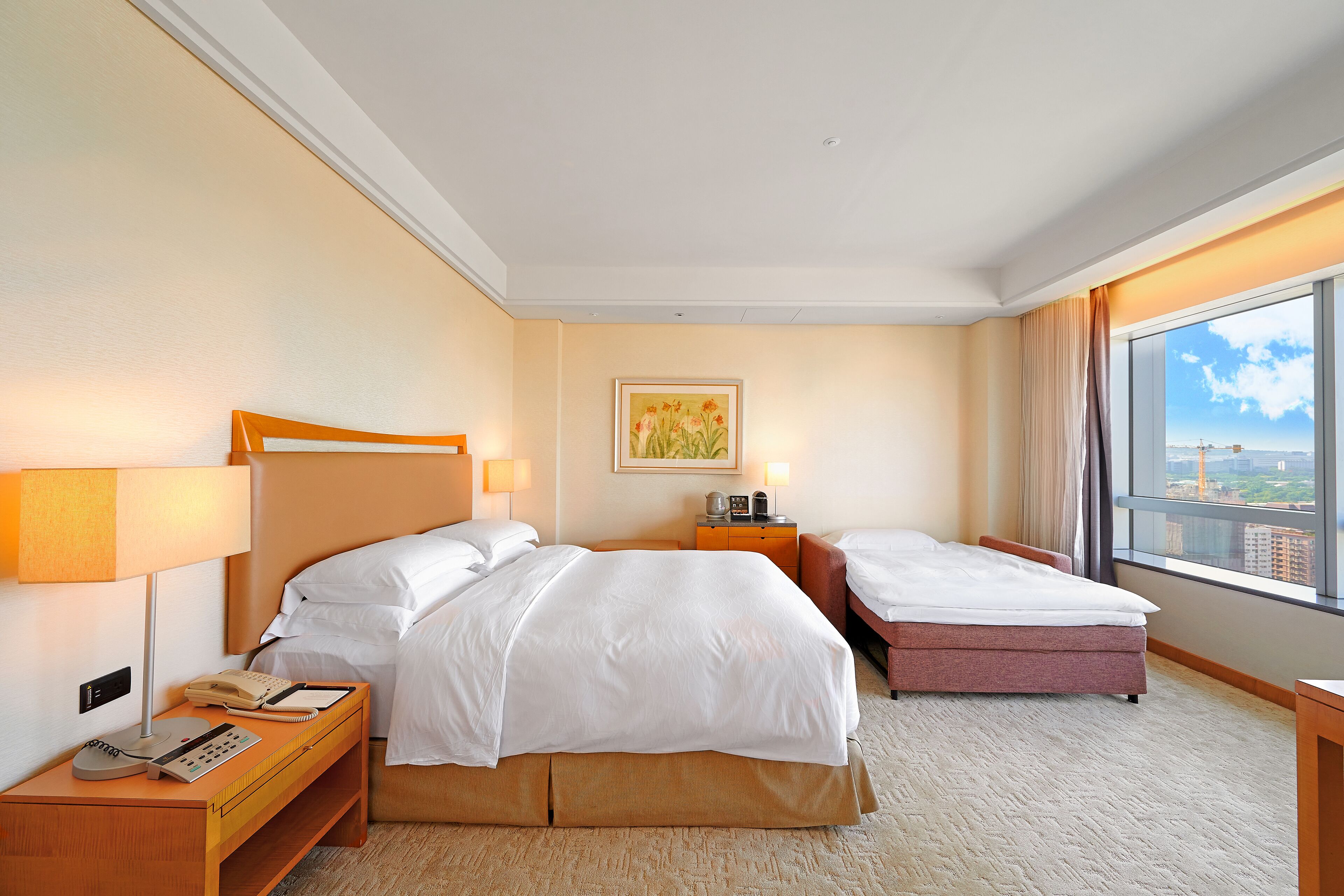 A hotel room with two beds, a desk with a telephone, a lamp, and a painting on the wall.