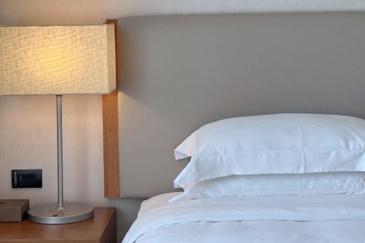 Una cama bien tendida con sábanas blancas y una mesita de noche con una lámpara.