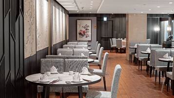 A modern restaurant with round tables and grey upholstered chairs, featuring a wooden floor and a large wall art piece.
