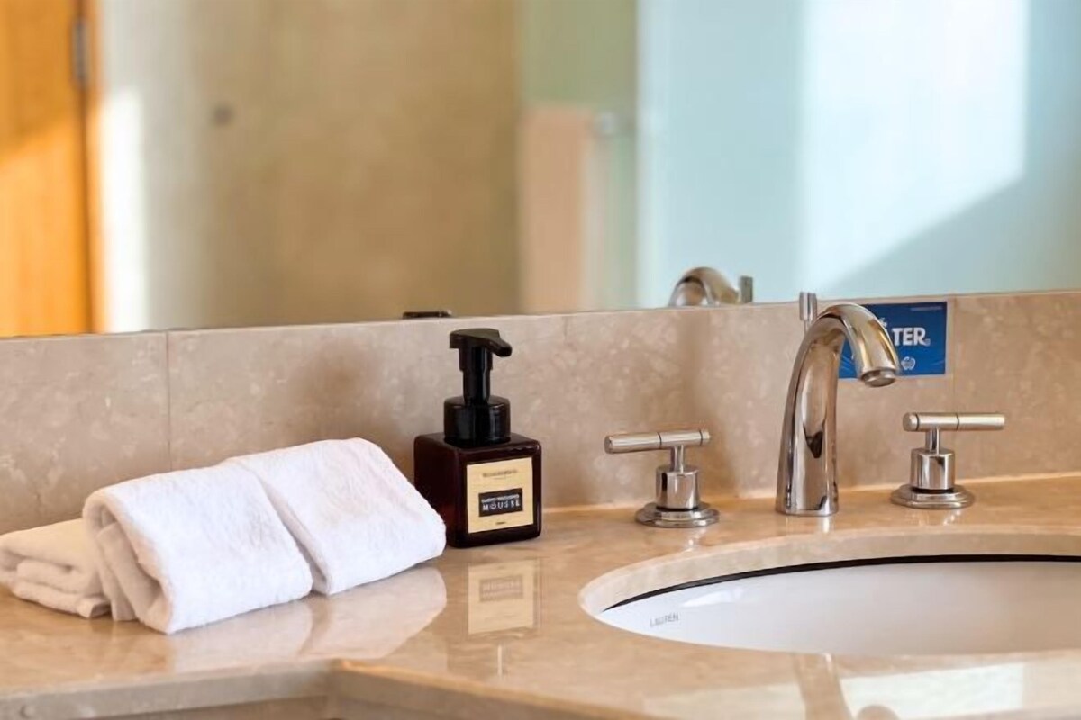 A bathroom with a sink, a mirror, a towel, and a soap dispenser.