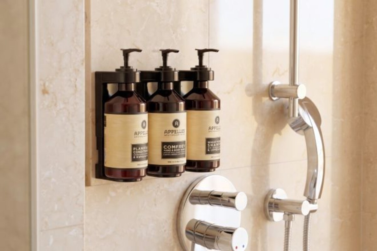 Un baño con ducha, un espejo y tres botellas de champú y acondicionador.