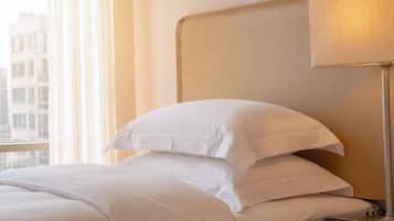 Habitación de hotel con cama, almohadas, lámpara y control remoto sobre una mesita de noche.