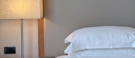 A neatly made bed with white linens and a modern floor lamp beside it.