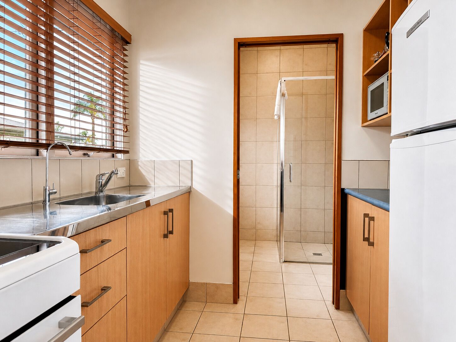 Una cocina moderna con lavabo, armarios y puerta de ducha de cristal.