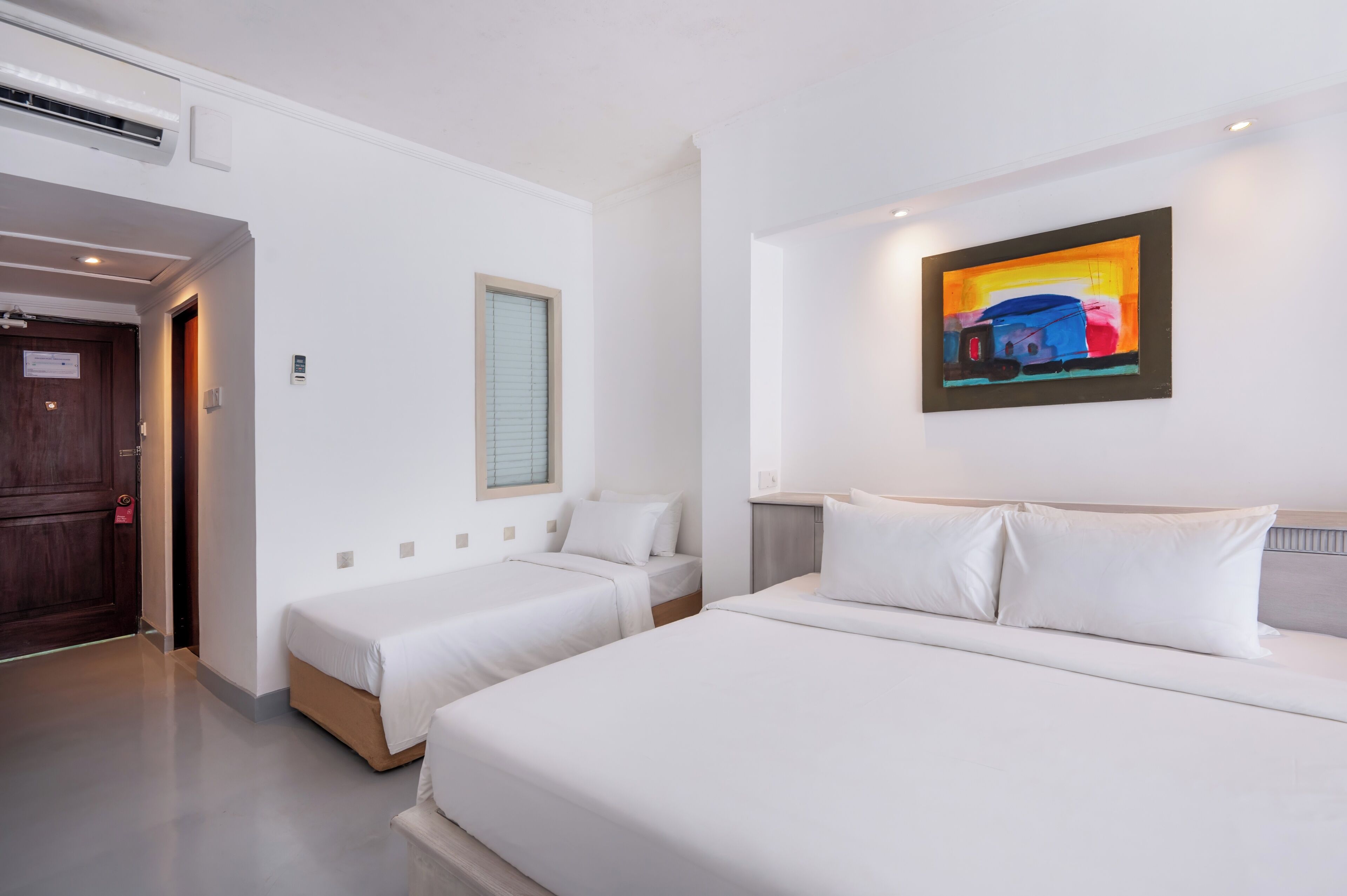 Ein Hotelzimmer mit zwei Einzelbetten, einem großen Bett, einem Bild an der Wand und einer Tür mit einem Schild.