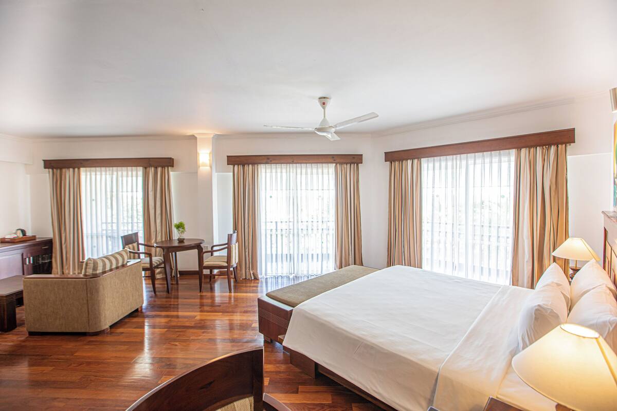 Habitación de hotel con una cama grande, un escritorio, una silla y un balcón con cortinas.