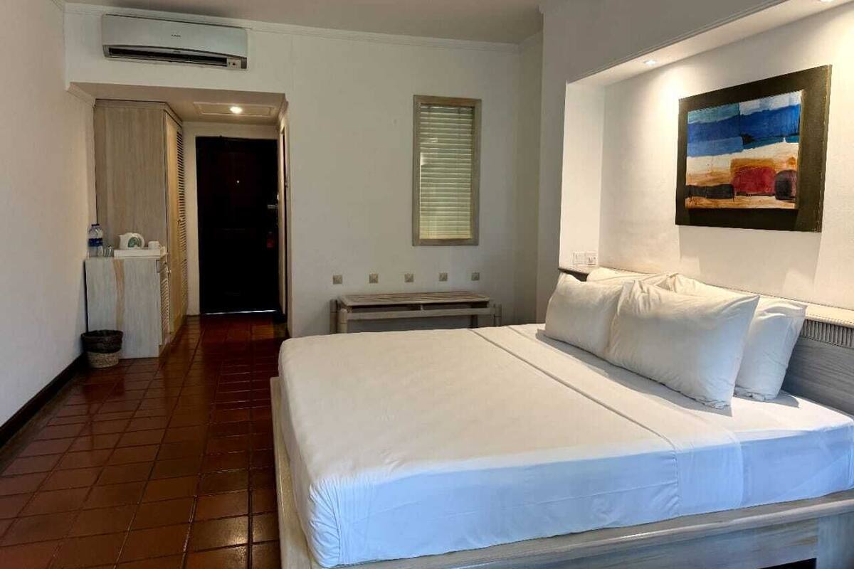 Una habitación de hotel con cama, un cuadro en la pared y un equipo de aire acondicionado.