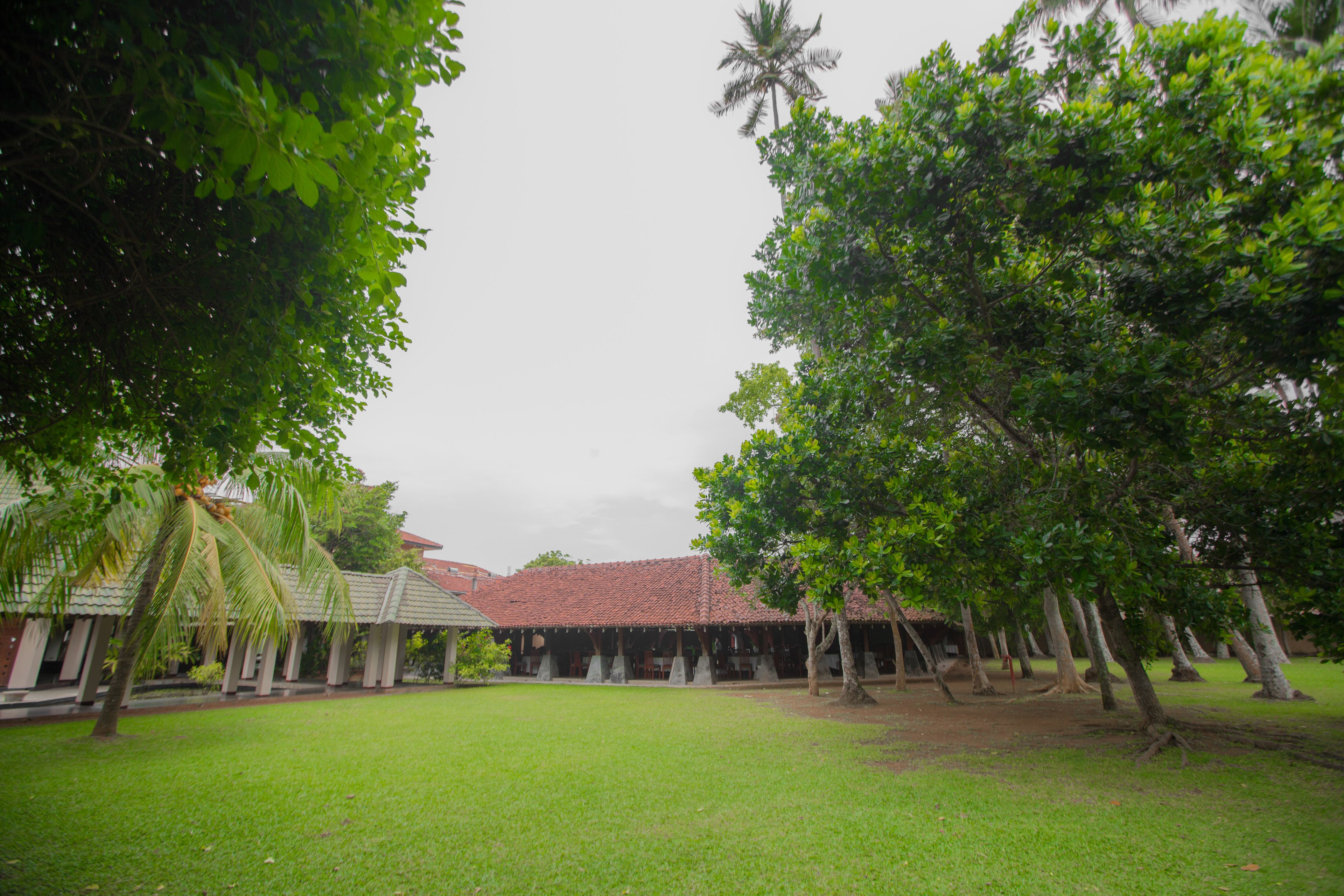 A courtyard with a red-tiled roof building, surrounded by lush green trees and a well-maintained lawn.